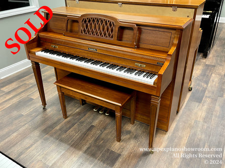 An upright Baldwin piano with a wooden finish and open sheet music holder, positioned in a showroom with laminate flooring.