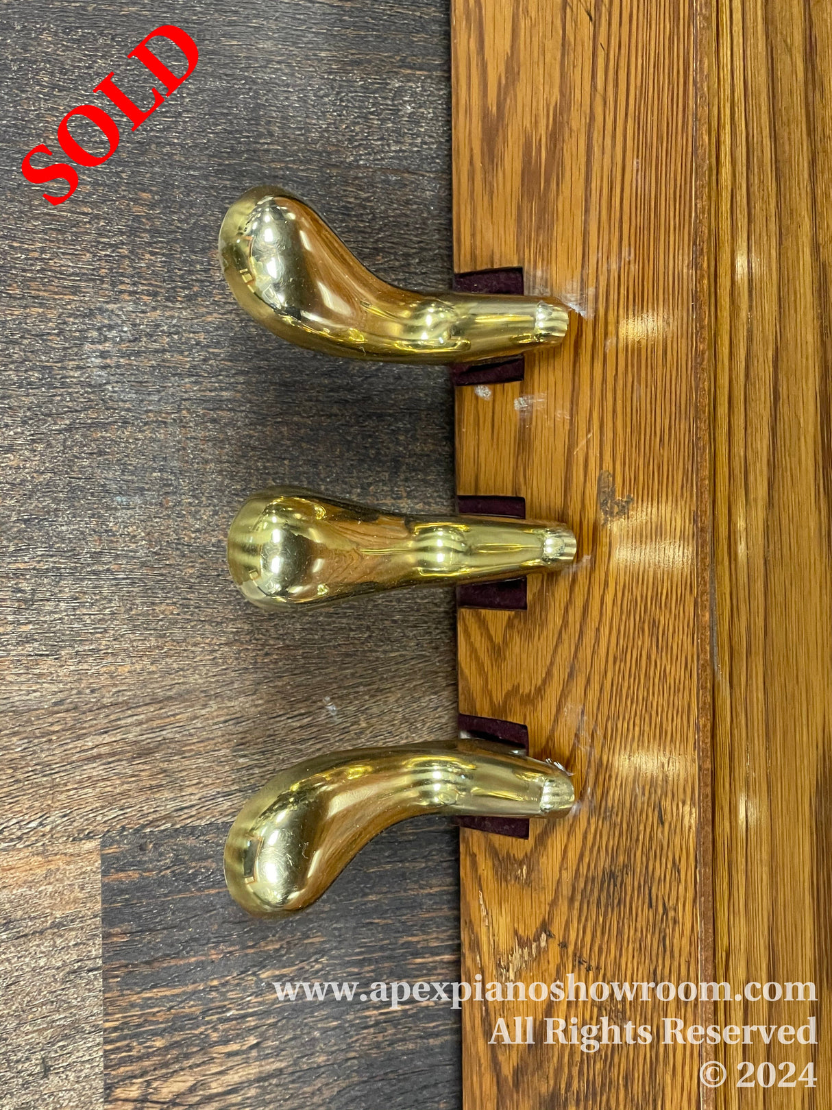 Glossy golden piano legs with casters attached to the bottom of a wooden piano, showcasing crafted curvature and polished finish on a hardwood floor.