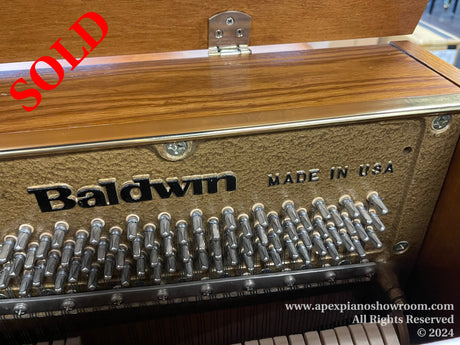 Interior of a Baldwin piano showing the tuning pins and strings with the brand name and MADE IN USA label visible, indicating the pianos manufacture origin.