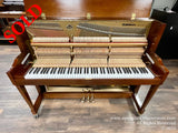 Open Baldwin upright piano displaying its internal mechanism including hammers and strings, set in a showroom with wood flooring.