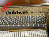 Interior view of a Baldwin piano showcasing its hammer mechanism and strings, with the brand name Baldwin and MADE IN USA visible, indicative of its American craftsmanship, set above the instruments white and black keys.