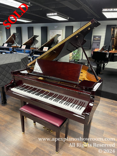 Polished mahogany grand piano with open lid on display in a showroom with a matching bench, amidst other grand pianos in the background, on a wooden floor.