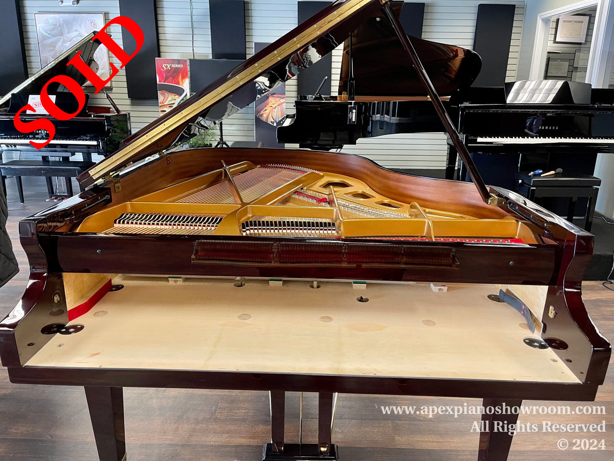 A polished grand piano with the lid open showcasing the intricate internal strings and hammers, set in a piano showroom with various other pianos in the background.