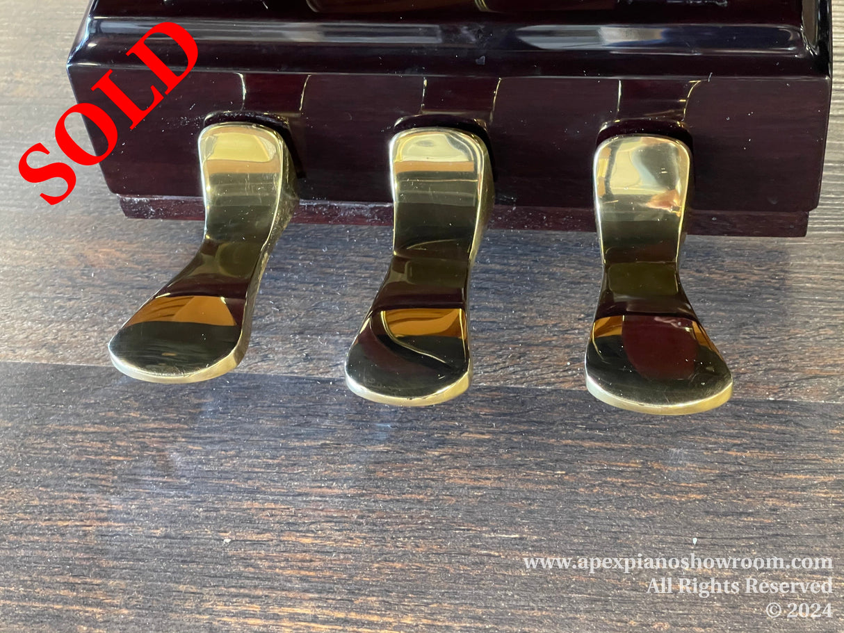 Three polished piano pedals on a dark wood finish grand piano, reflecting light on a wooden floor.