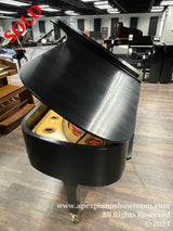 A black grand piano with its lid open, showcasing the golden interior mechanics and strings, situated in a showroom with various other pianos in the background.