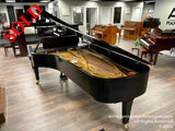 A grand piano with a glossy black finish and open lid, revealing its golden interior, in a well-lit showroom with various upright pianos in the background.