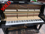An upright piano with its front panel removed, exposing the hammers and strings, model EUP-123, situated in a showroom.