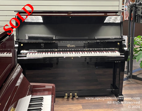 A glossy black Essex upright piano with white keys and the lid open, located in a well-lit showroom with hardwood floors and adjacent pianos partially visible.
