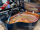 A selection of grand pianos on display in a showroom, with a focus on a shiny black grand piano with its lid open revealing its strings and hammers, surrounded by other pianos, likely in a piano store or showroom setting.