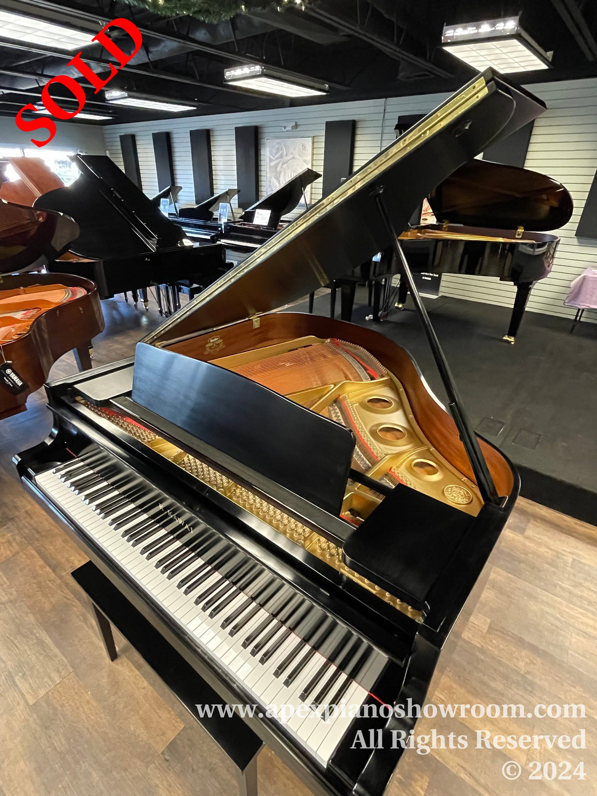 A grand piano with an open lid displaying its internal strings and hammers, situated in a showroom with multiple pianos in the background.