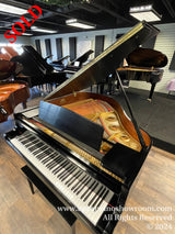 A grand piano with an open lid displaying its internal strings and hammers, situated in a showroom with multiple pianos in the background.