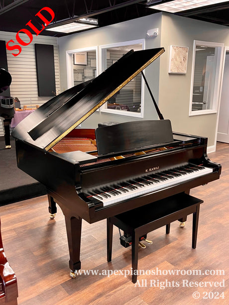 A gleaming black grand piano by Kawai with the lid open, displaying its intricately constructed interior, situated in a well-lit, modern showroom with wooden flooring and light gray walls.