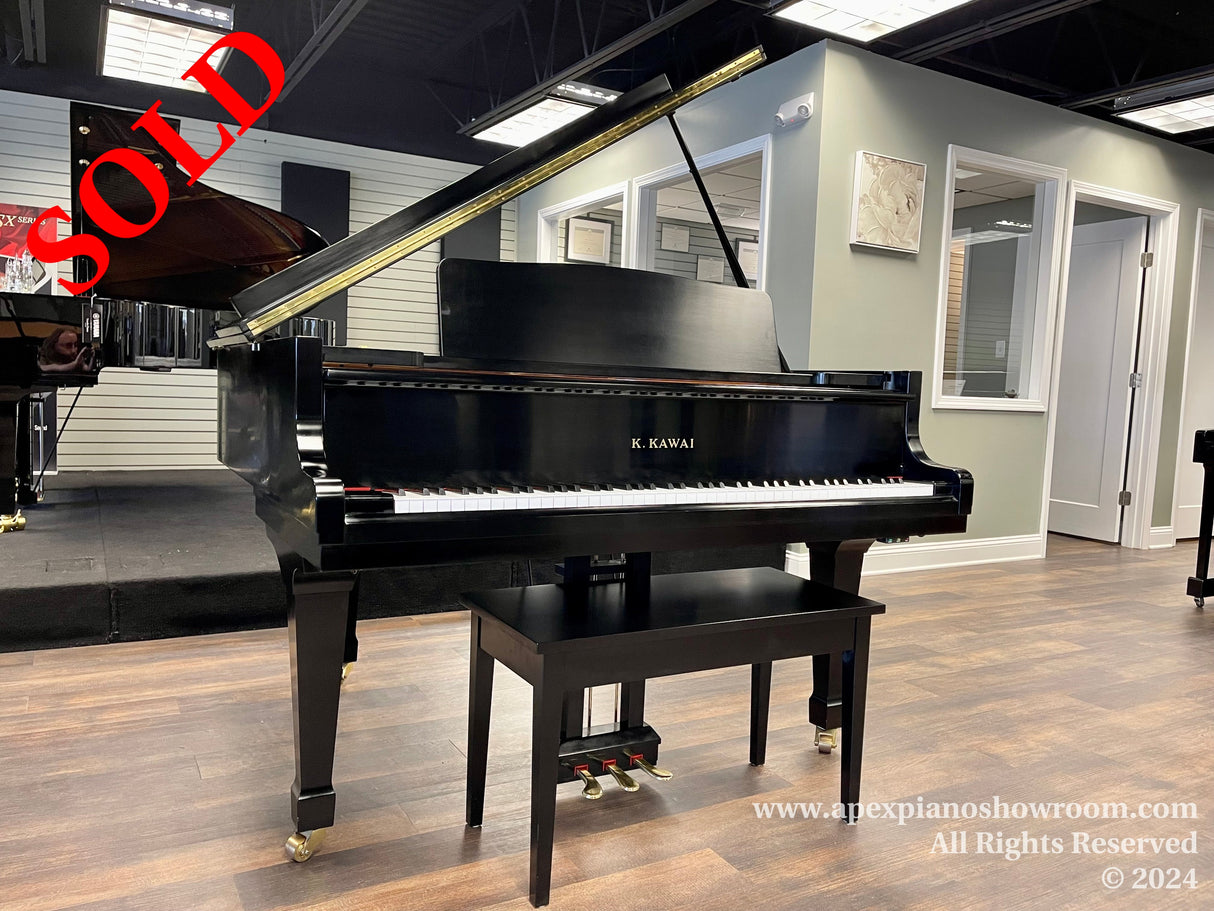 A shiny black Kawai grand piano with an open lid on display in a well-lit piano showroom, featuring elegant brass casters and a matching piano bench.