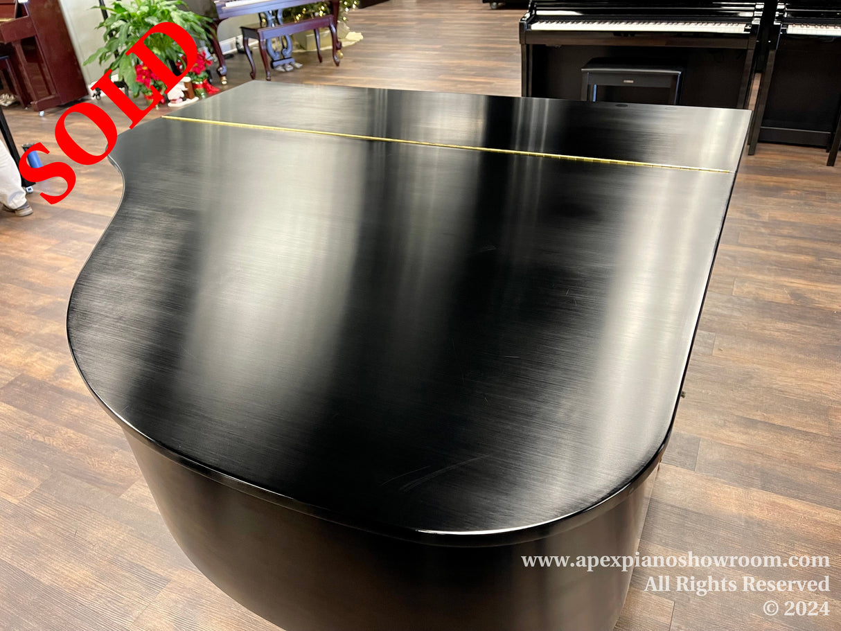 A polished black grand piano with a sleek finish is showcased in a piano showroom with wood flooring, flanked by other pianos in the background, alluding to a diverse selection for buyers.