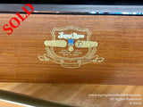 Close-up view of the wood grain finish on a Kawai piano, featuring a golden emblem with text indicating the brand, musical instrument status, and Japanese manufacturing origin.
