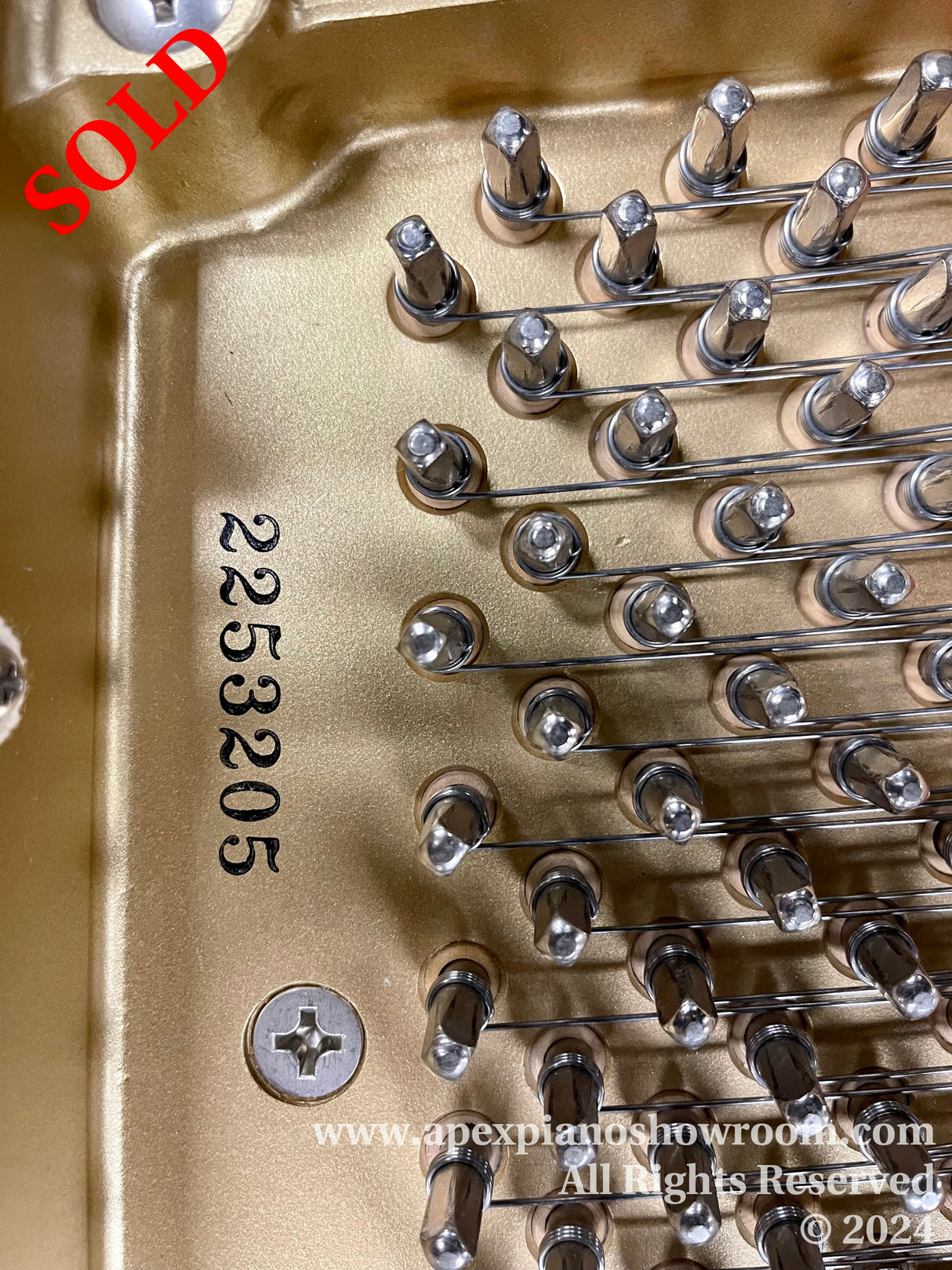 Close-up of a piano's gold-painted cast iron plate showing tuning pins and strings, along with a serial number 2523205 imprinted on the plate, indicative of precision engineering in piano manufacturing.