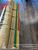 An array of disassembled piano keys and action mechanism parts laid out on a hardwood floor in a piano showroom, showcasing the intricate internal components that produce the instruments sound.