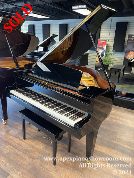 A glossy black grand piano with its lid open, positioned in a well-lit piano showroom with other pianos in the background, displayed on a wooden floor.