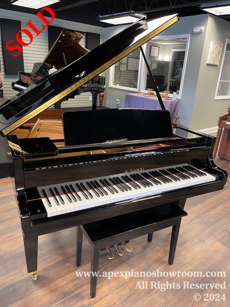 A shiny black Kawai grand piano with lid open, displayed in a piano showroom with wood flooring and soft lighting.