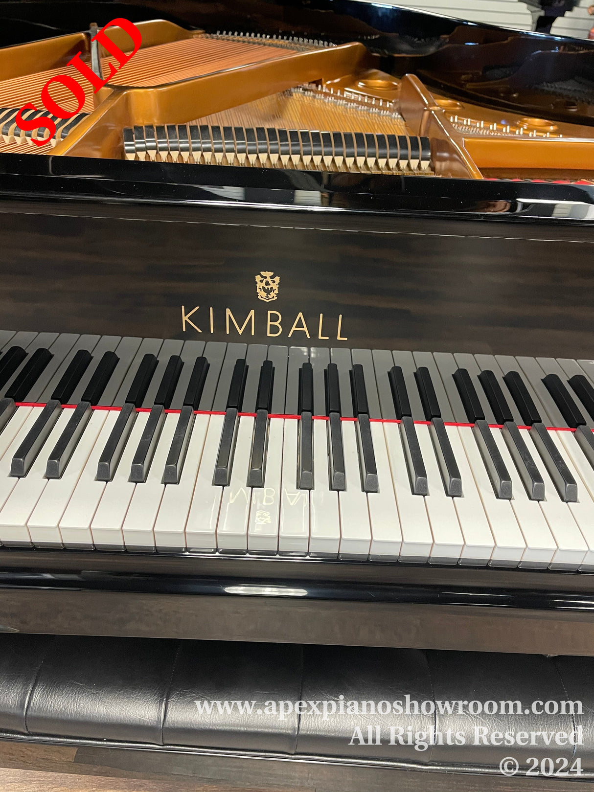 A glossy black Kimball grand piano with a visible brand logo, showcasing white and black keys and the interior golden harp and strings, on a showroom floor.
