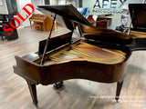 A grand piano with a rich, mahogany finish, lid propped open, showcasing its strings and hammers inside, situated in a well-lit piano showroom with other pianos in the background.