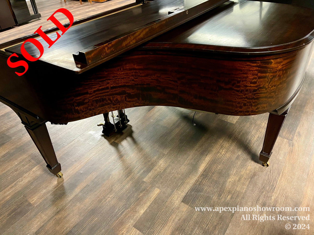 Elegant grand piano with glossy, figured wood finish and curved legs on a hardwood floor, indicative of high-quality craftsmanship in piano manufacturing.