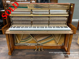 Upright piano with exposed interior showing strings and hammers, set in a showroom with wooden flooring.