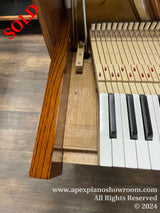 Close-up view of a pianos wooden finish, hammer action mechanism with numbered parts, and a portion of black and white keys showcasing the interior and craftsmanship of a piano.
