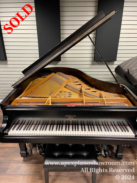 Grand piano with open lid showcasing internal strings and hammers, with Steinway & Sons branding visible, set against a striped wall in a showroom.