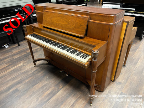 A classic wooden upright piano with decorative legs displayed in a showroom surrounded by other pianos.