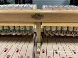 Close-up view of a piano action mechanism with the brand Aetion since 1908 on a wooden rail, showcasing felted hammers and damper felts against piano strings.