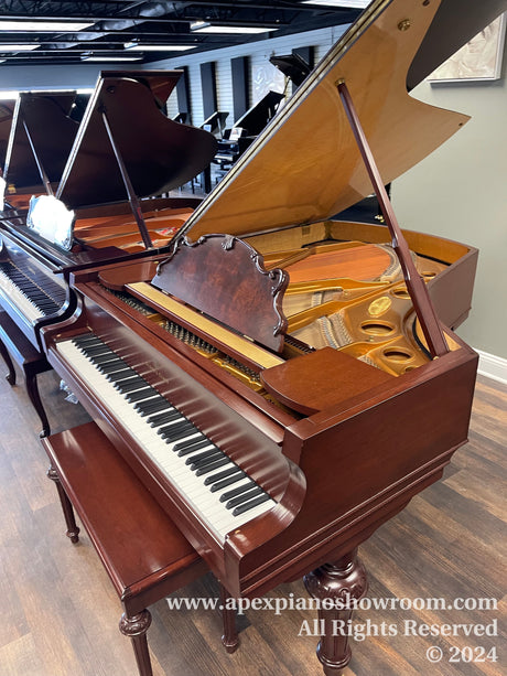 An elegant mahogany grand piano with the lid open displaying its strings and hammers, situated in a showroom with other pianos in the background, reflecting careful craftsmanship and design typical of high-quality musical instruments.