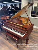 An elegant grand piano with a polished mahogany finish, featuring an open lid that reveals its intricate internal strings and soundboard, positioned inside a well-lit piano showroom with decorative elements, such as a music stand and wall art, reflecting the high-end nature of the instrument.