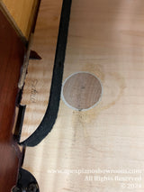 Close-up view of water damage on the inner wooden components of a piano, displaying discoloration and a watermark on the soundboard.
