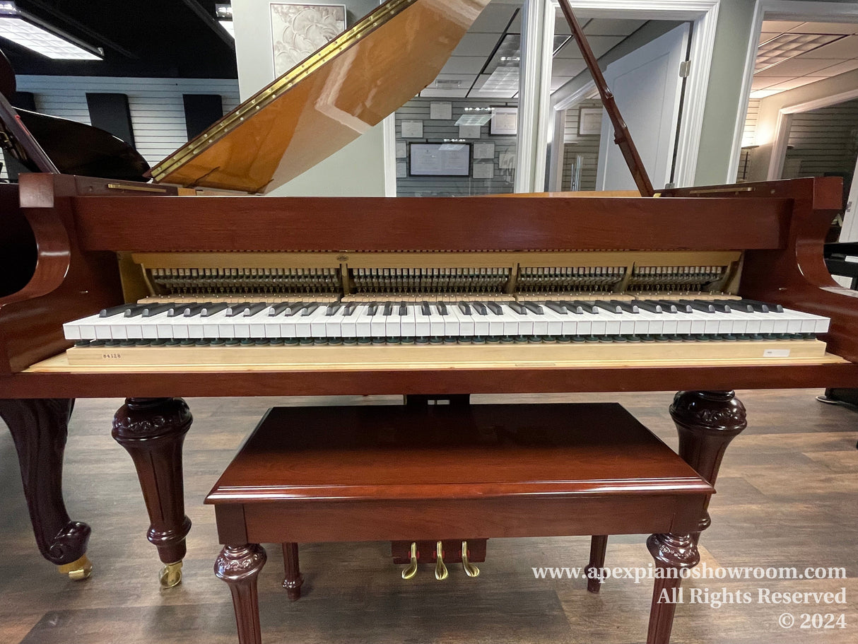 A grand piano with its lid open, showcasing the interior strings and hammers, keys poised for play, and a polished mahogany finish supported by ornately carved legs with caster wheels for ease of movement, set in a showroom environment.
