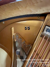 Close-up view of the interior of a grand piano showing string details, the number 65, and gold-painted frame, with a birdseye maple pin block, emphasizing the craftsmanship and design of the instrument.