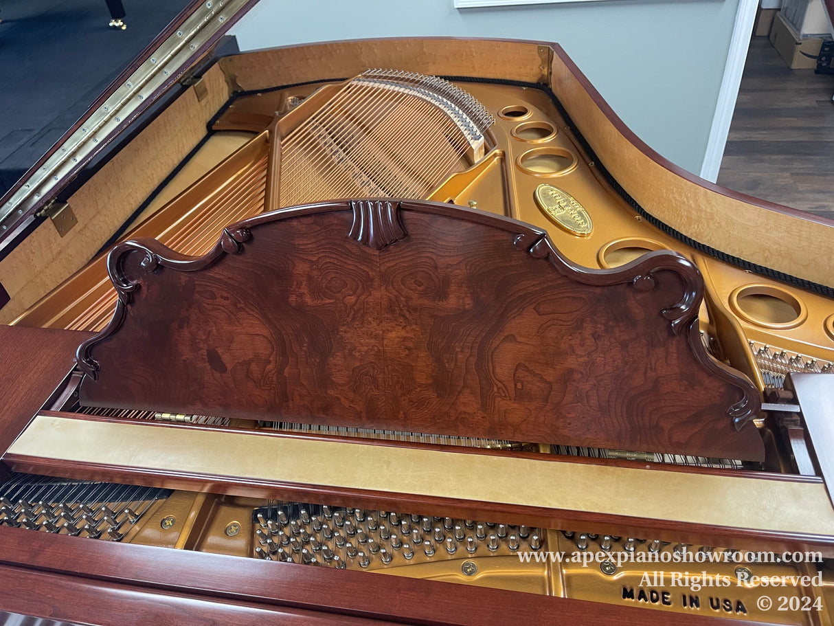 A grand piano interior showcasing the intricate string arrangement, the shiny gold-painted iron frame with a manufacturers emblem, and a highly polished mahogany music desk with decorative carvings.