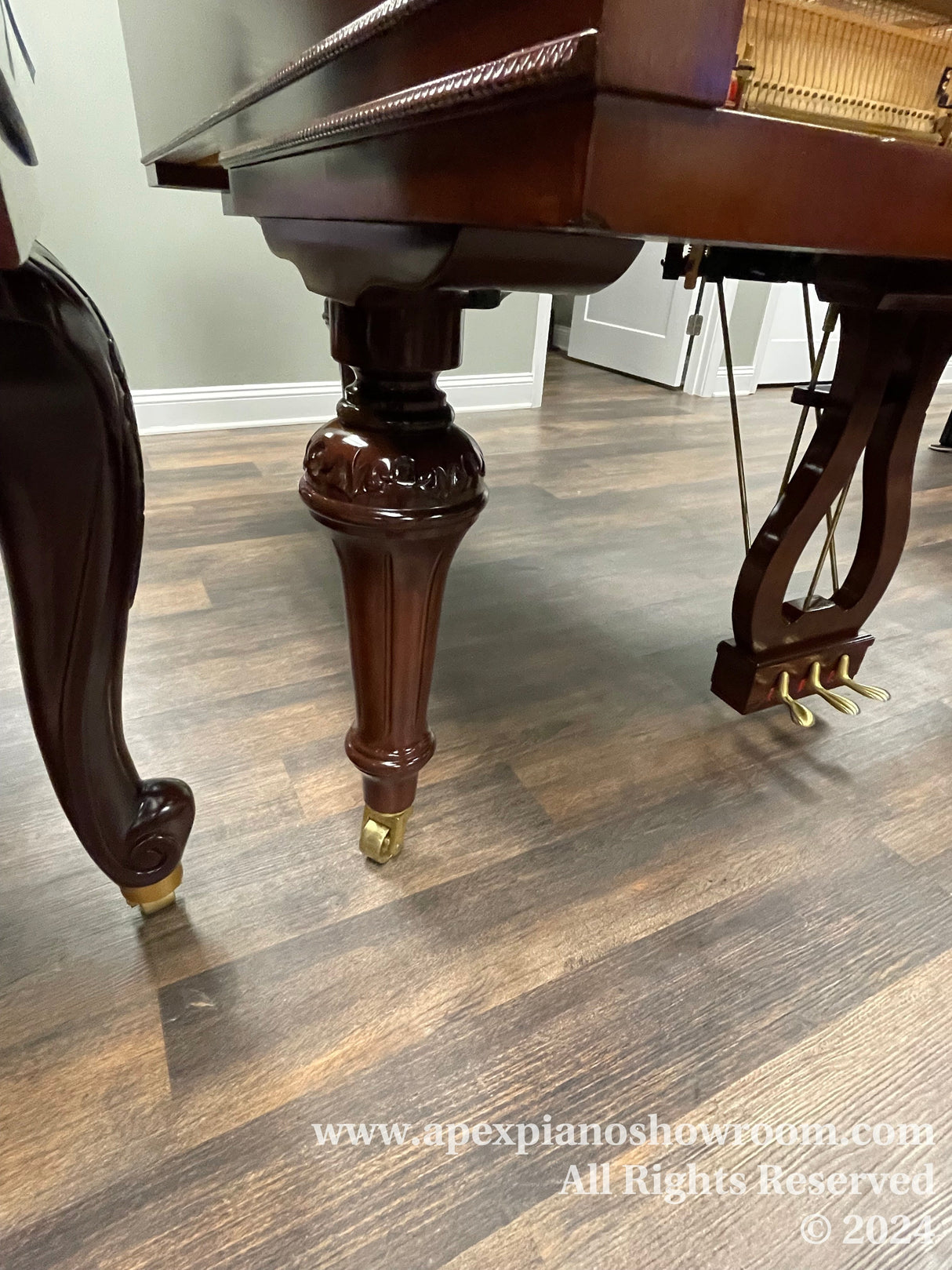 Close-up view of the elegantly carved legs and casters of a polished mahogany grand piano, highlighting the craftsmanship and stability features designed for easy positioning within a showroom or home environment.