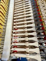 Interior view of a piano showing the intricate alignment of hammers and dampers, with red felt and wooden structures visible, illustrating the complexity and precision of piano mechanics.