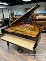 A grand piano with its lid open revealing the intricate inner strings and hammers, set in a piano showroom with various types of keyboards and organs in the background.