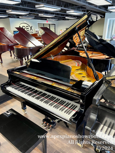 A black grand piano with the lid open, showcasing the strings and interior mechanics, in a showroom surrounded by other grand pianos.