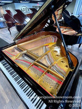 Interior of a grand piano showing strings and hammers, with other grand pianos in the background at a piano showroom.