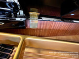 Interior view of a grand piano showing the gold colored frame, strings, and the wood finish beneath the pianos lid, with a focus on the pianos hardware and craftsmanship.