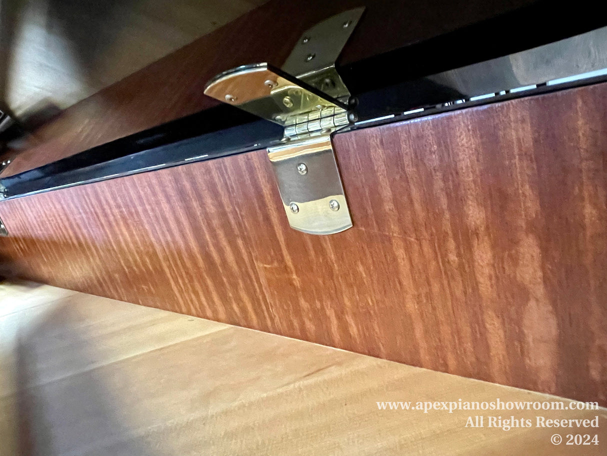 Close-up view of a grand piano fallboard lock and hinge, featuring a polished wood finish and metal hardware, demonstrating the security and craftsmanship of piano design.
