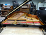A grand piano with its lid open, showcasing its strings and hammers, sits in a showroom with various electronic organs and speakers in the background.