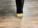 Black piano leg with brass caster on wooden floor.