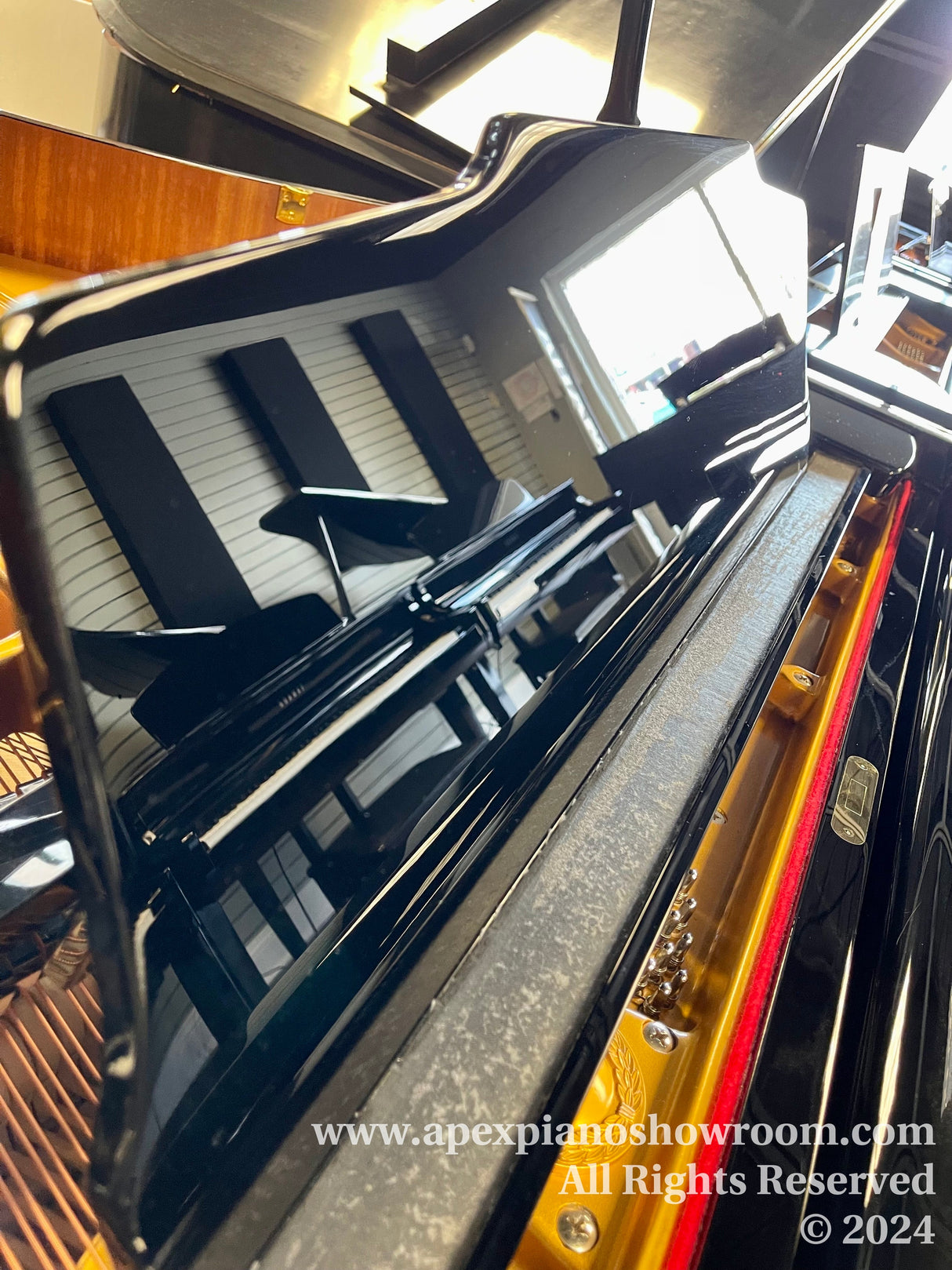 A glossy black grand piano with its lid open, showing the strings and hammers inside, reflecting the keyboard and the bright room its situated in.