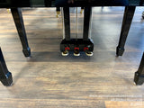 Close-up of a grand pianos black legs and shiny gold casters on a wooden floor.