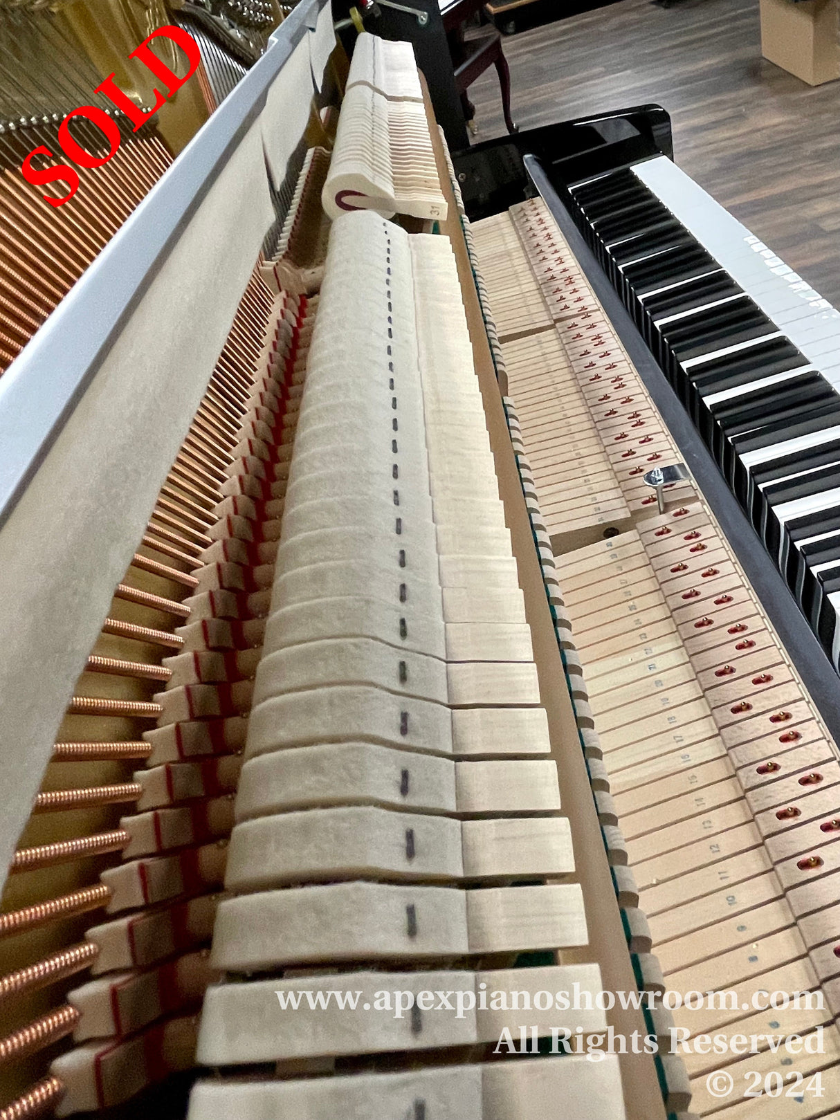 Interior view of a grand piano showing the hammers and strings, with focus on the dampers and the keyboard, located in a showroom.