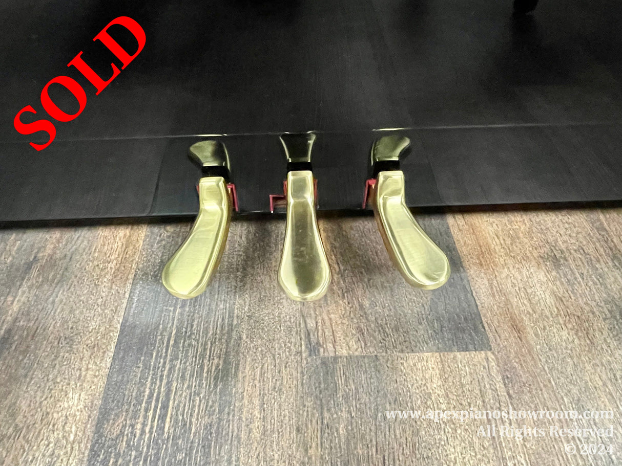 Close-up view of three brass piano pedals on a glossy black grand piano, showcasing their reflective surfaces and ergonomic shapes designed for nuanced musical expression.